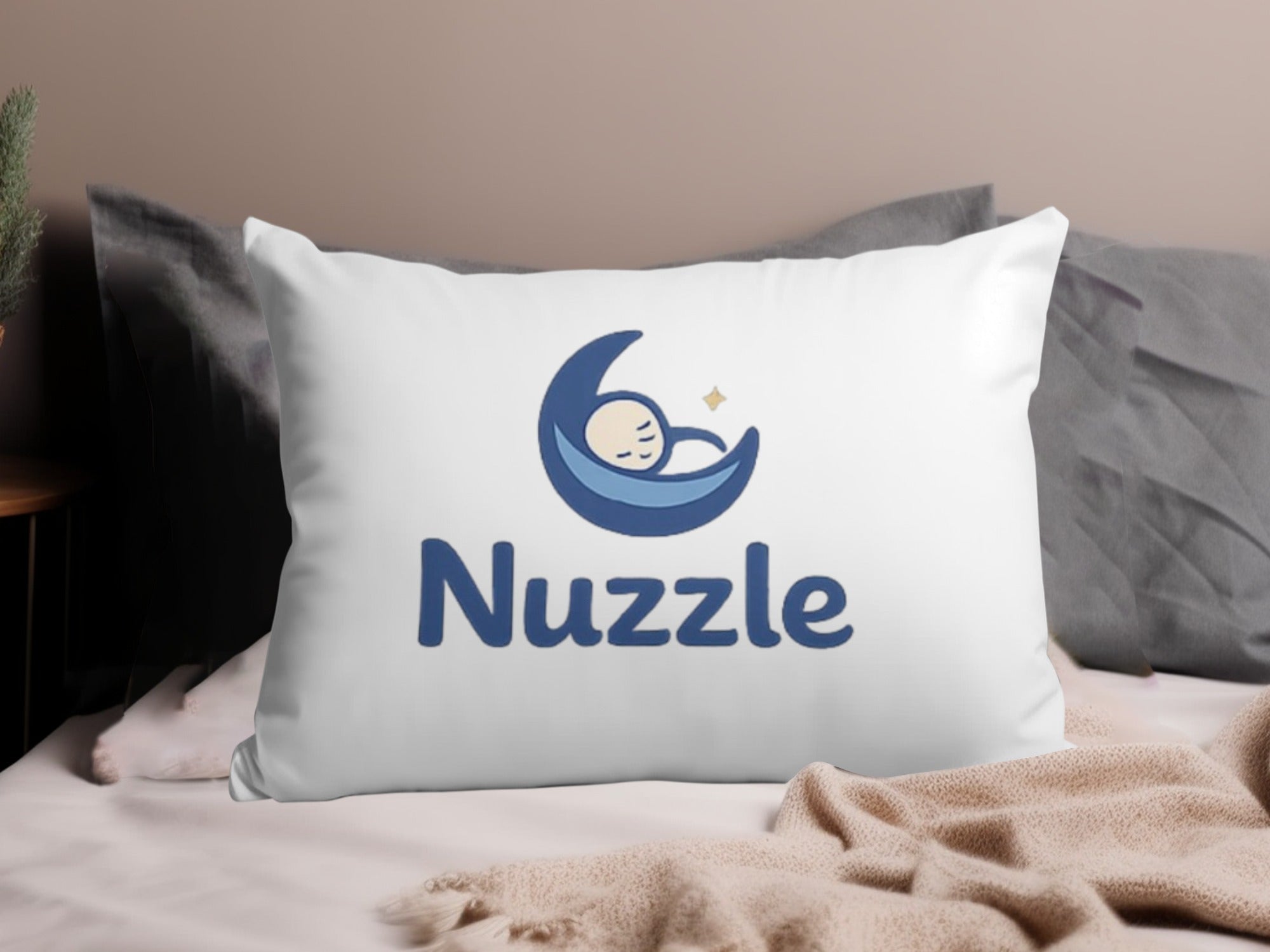 White pillow with Nuzzle logo featuring sleeping baby on moon.