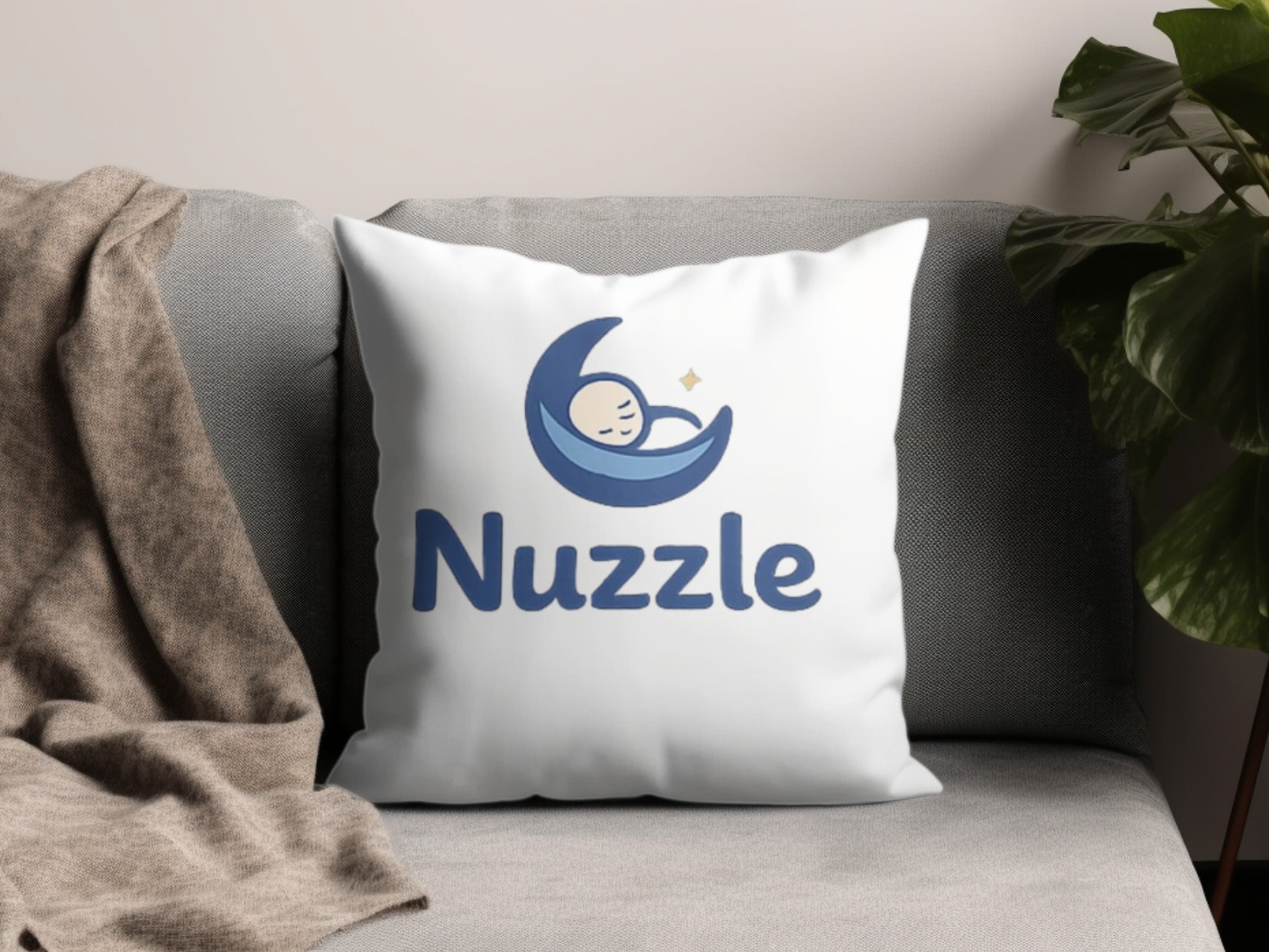 White pillow with blue "Nuzzle" logo featuring a sleeping baby in a crescent moon.