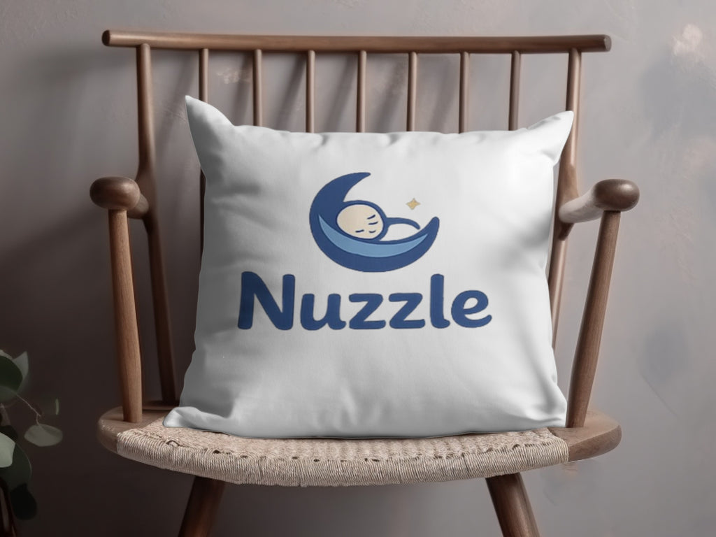 White pillow with blue "Nuzzle" text and baby moon logo on wooden chair.